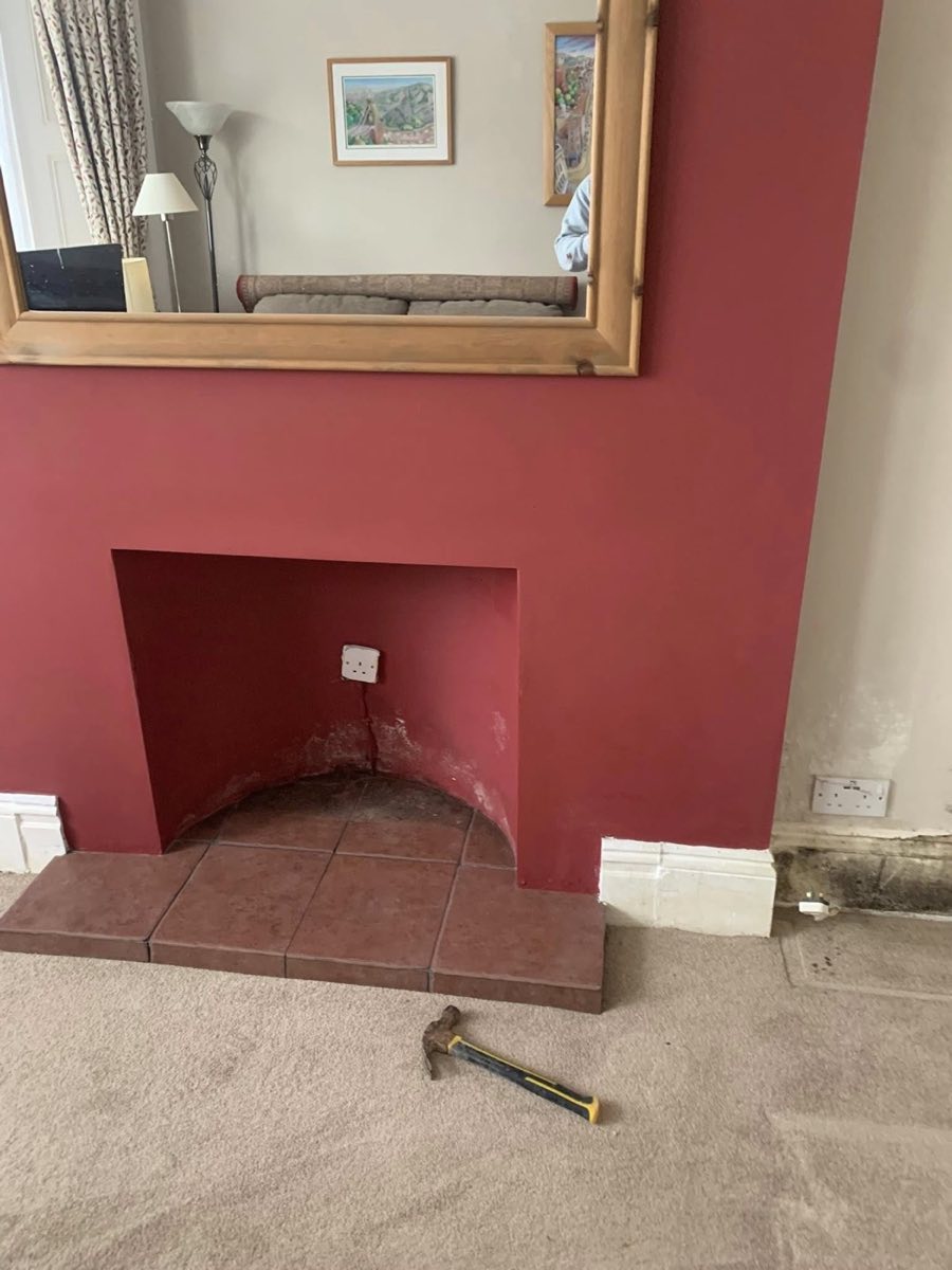 Chimney breast before treatment, with damp staining and spoiled paint along the skirting board beside a blocked fireplace