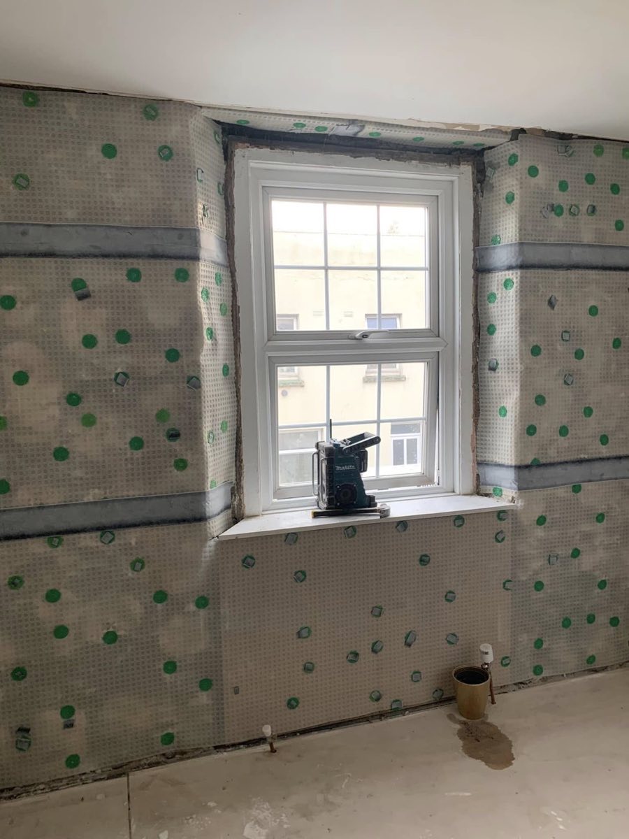 A room with damp-proof membrane fixed across the walls and window reveal, taped at the joints, ready for rendering