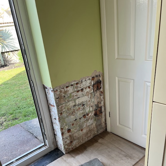 The corner beside a patio door taken back to bare brickwork at low level around the threshold