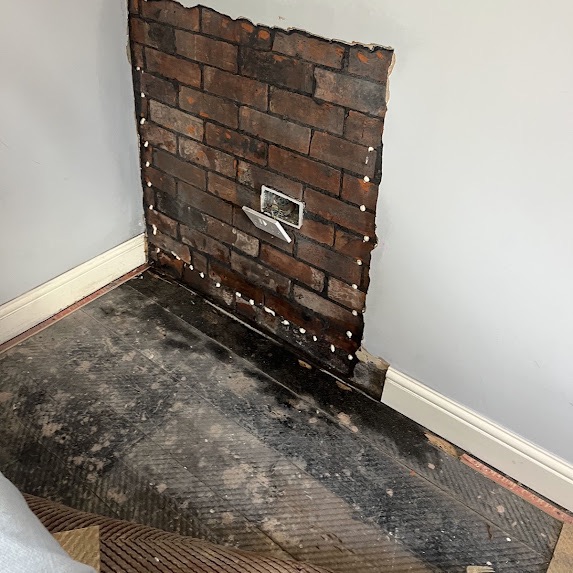 A corner hacked back to brick with damp-proof course injection plugs, a trowel in the wall and a damp-proof membrane laid over the floor