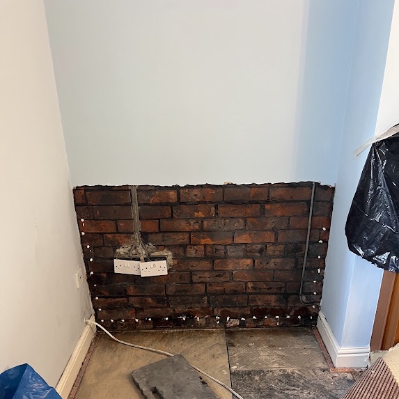 A wall hacked back to brick with two rows of white damp-proof course injection plugs along the mortar beds
