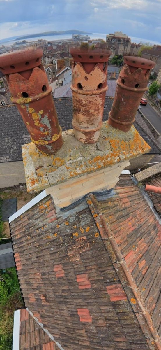 Drone view of a weathered brick chimney stack with cracked flaunching and lichen, Weston-super-Mare rooftops and the sea beyond