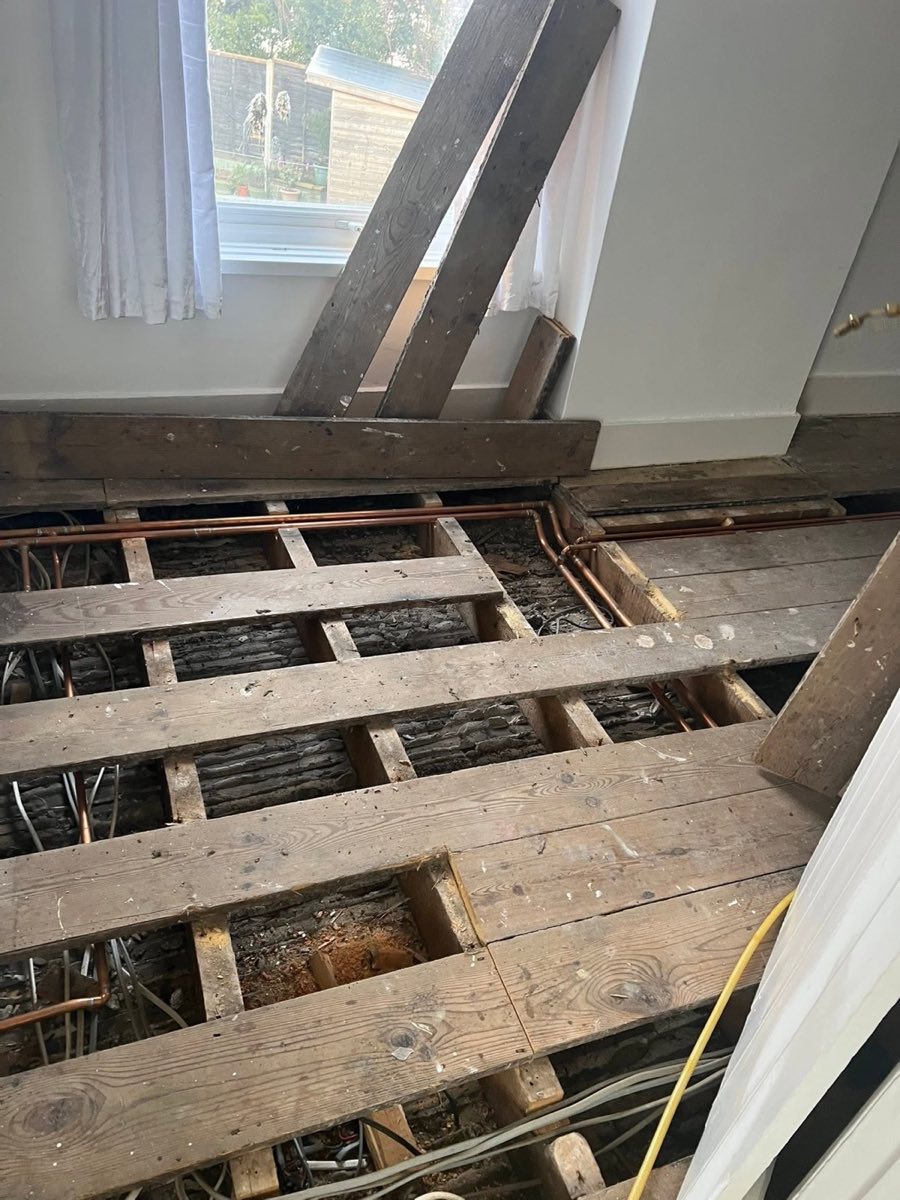 Floorboards lifted to expose the joists and sub-floor void, with some darkened timber visible