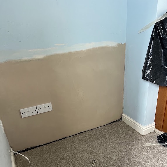 A wall re-rendered and skim-plastered smooth over the treated area, sockets reinstated, ready to decorate